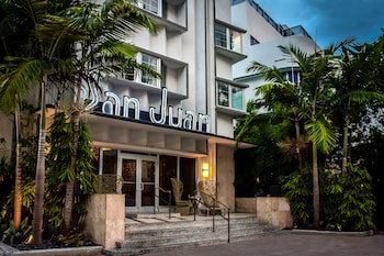 A swimming pool with lounge chairs and a building with a green ivy-covered wall and large windows. at San Juan Hotel