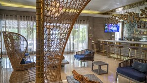A modern lounge area with wicker furniture, a bar with stools, and a television screen. - San Juan Hotel (Miami Beach)