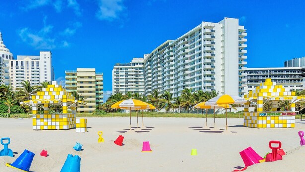 A beach with colorful play structures, umbrellas, and a food and beverage kiosk. - San Juan Hotel (Miami Beach)