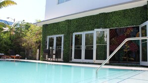 A swimming pool with lounge chairs and a building with a green ivy-covered wall and large windows. - San Juan Hotel (Miami Beach)