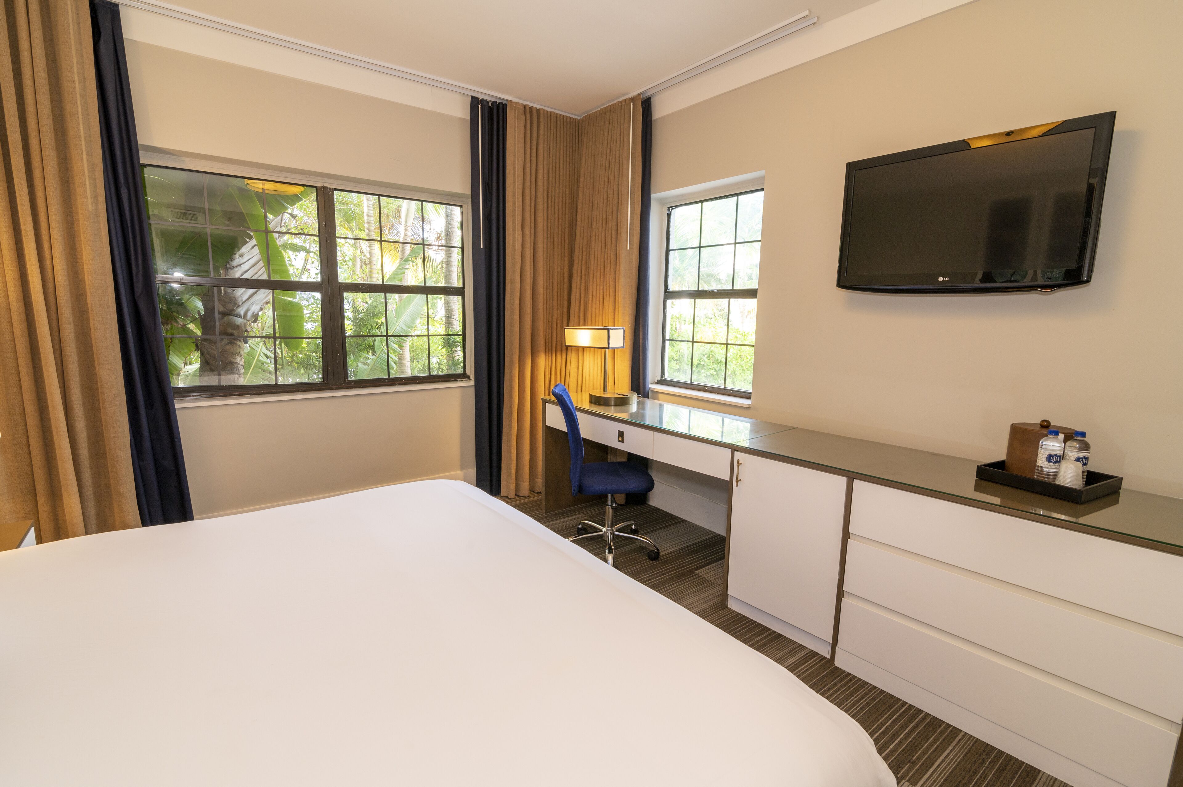 A hotel room with a bed, a desk with a chair, a TV, and a window with curtains.