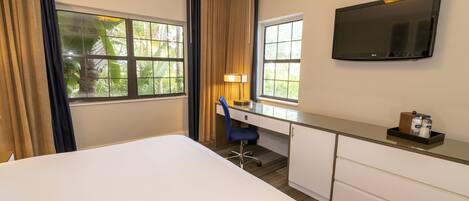 A hotel room with a bed, a desk with a chair, a TV, and a window with curtains.