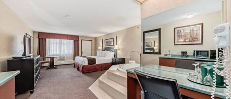 A hotel room with a bed, desk, and kitchenette.