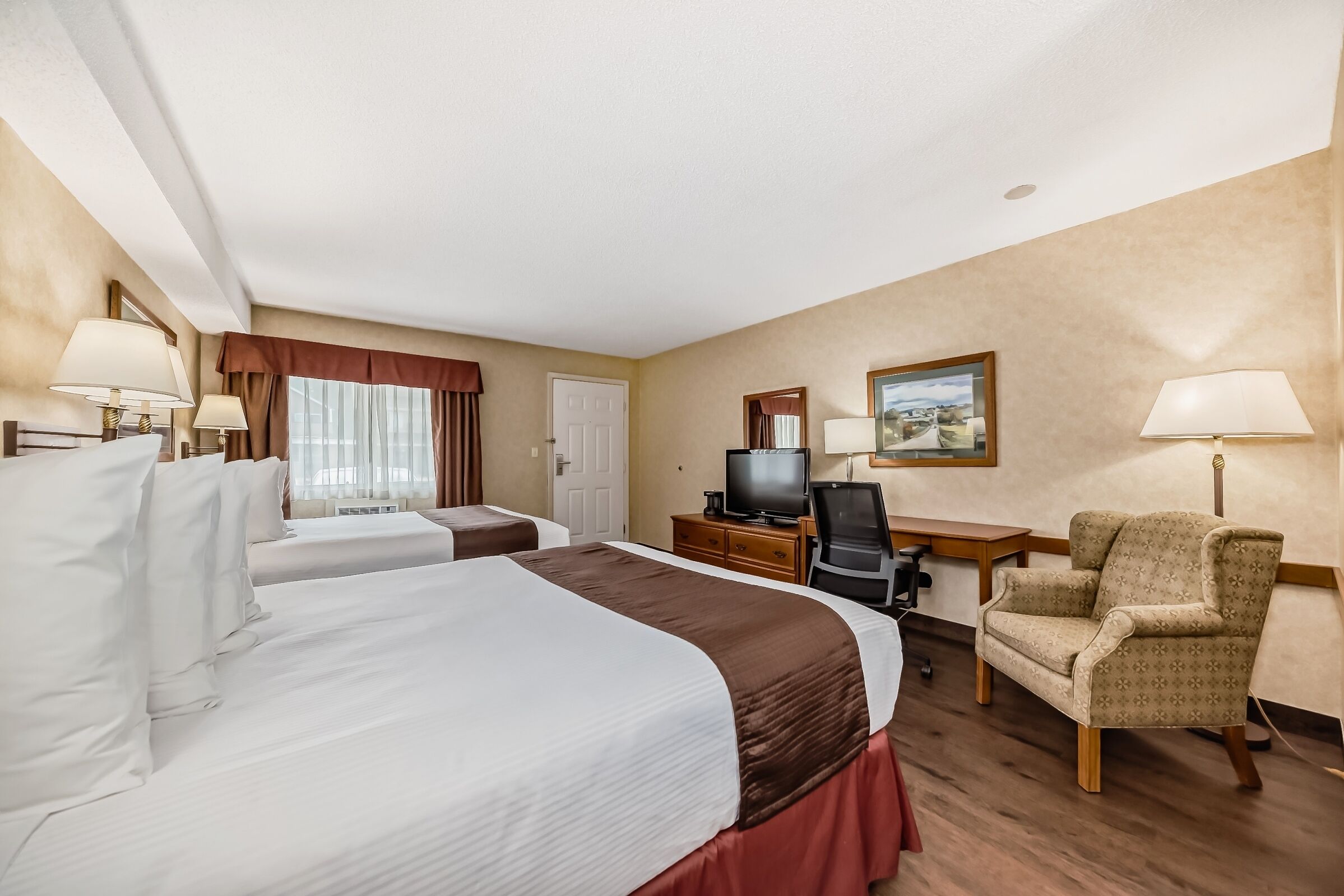 A hotel room with two beds, a desk, a chair, a television, and a painting on the wall.