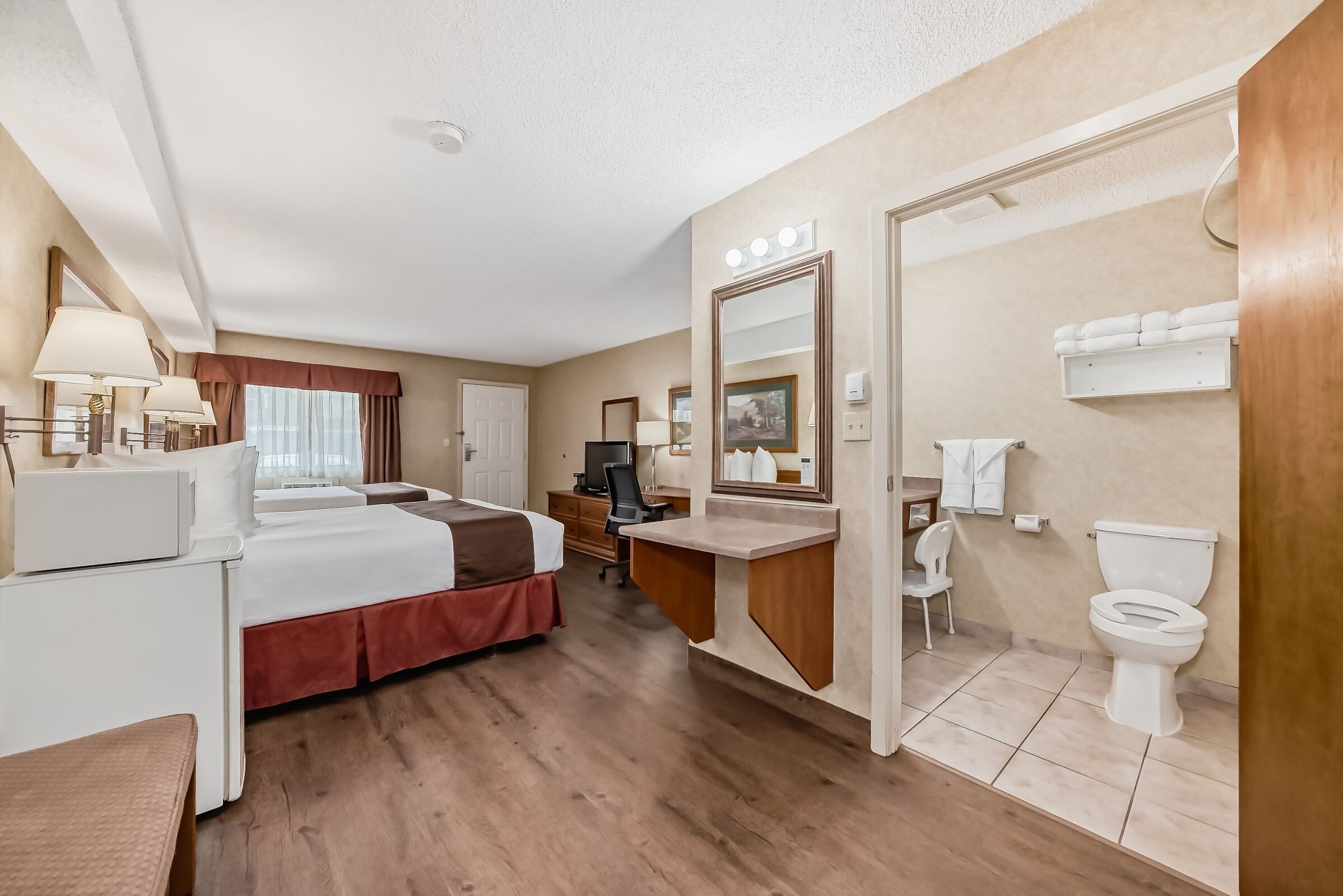 Une chambre d’hôtel comprenant un lit, un bureau, une chaise et une salle de bain avec des toilettes et un lavabo.