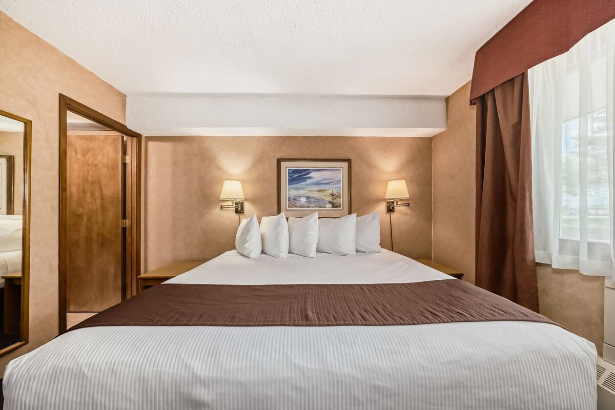 Une chambre d’hôtel avec un grand lit, deux lampes de chevet, un tableau au mur et une vue sur l’extérieur par la fenêtre.