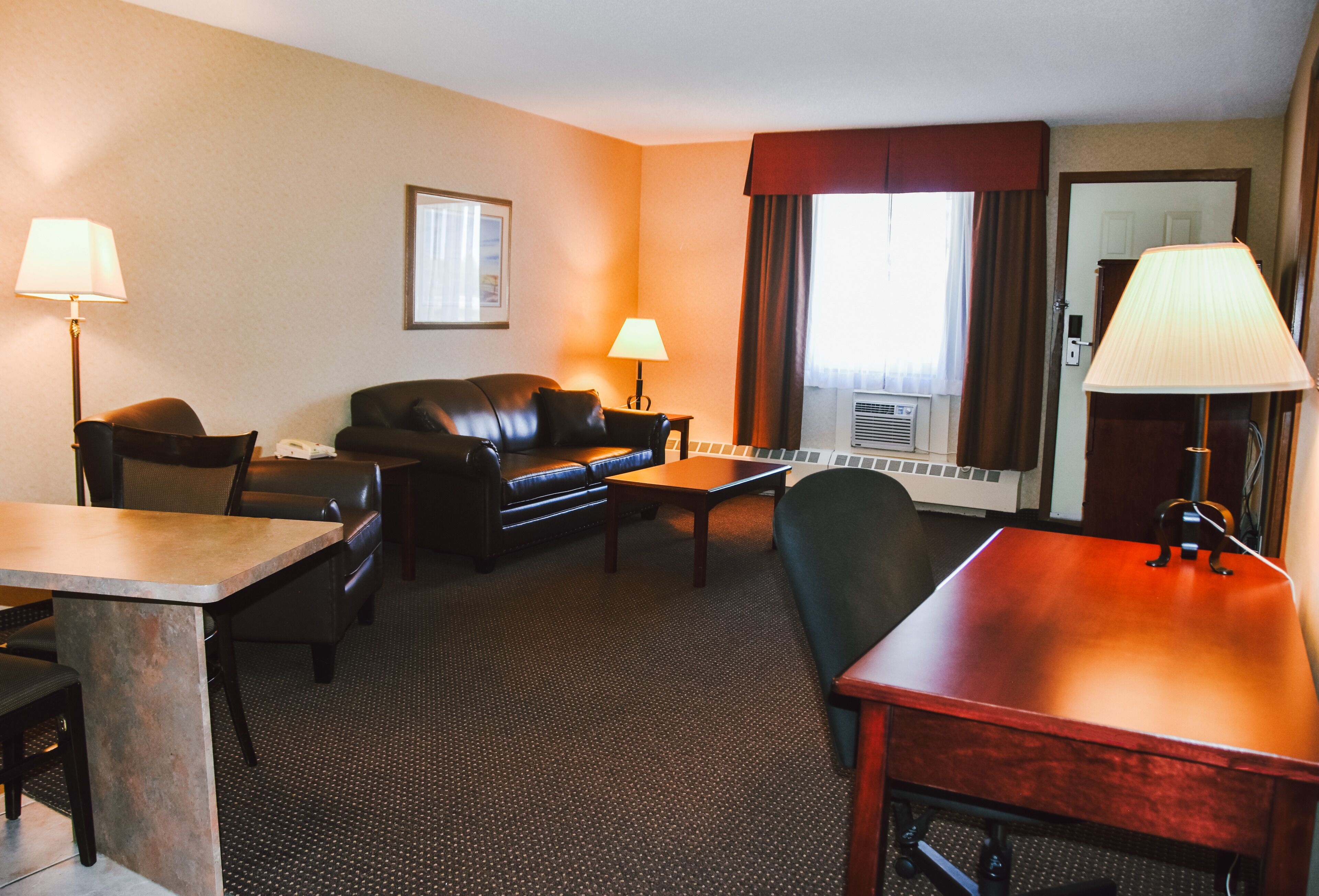 Une chambre d’hôtel comprenant un canapé, deux fauteuils, une table en bois, un bureau et deux lampes.