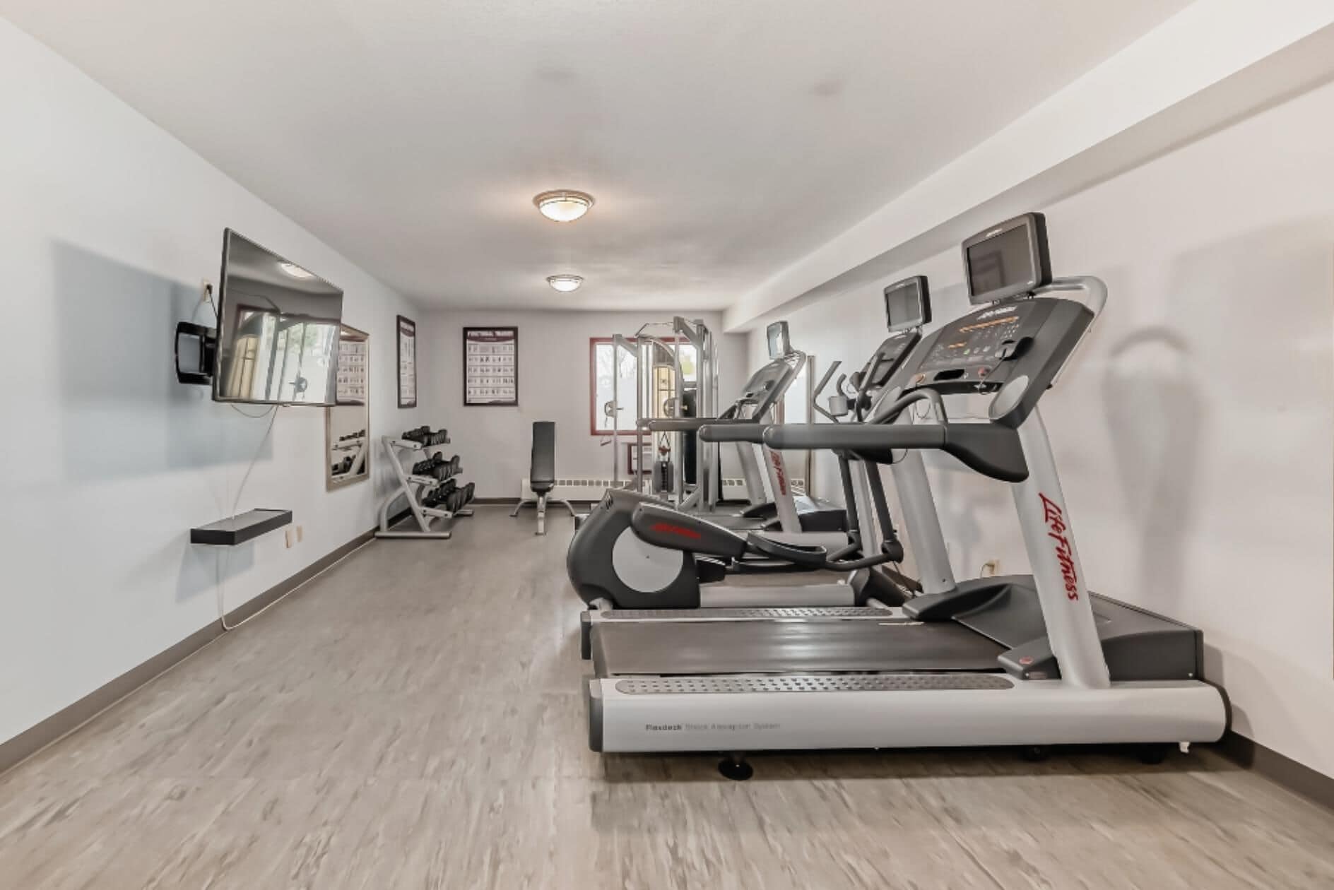Un gimnasio con cintas de correr, máquinas de pesas y un espejo.