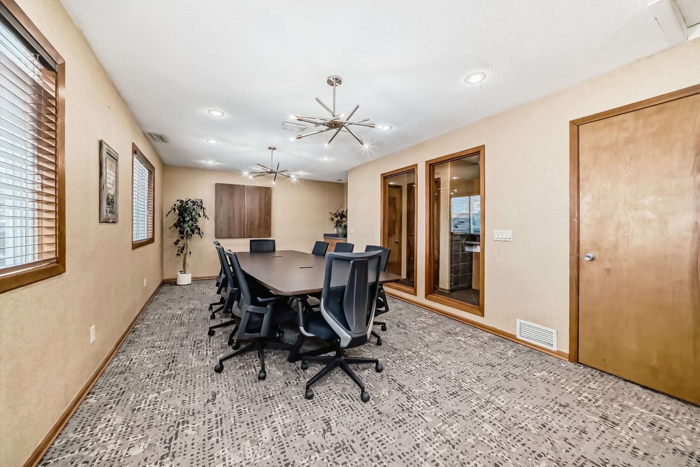 A conference room with a large table, chairs, ceiling lights, and a potted plant.