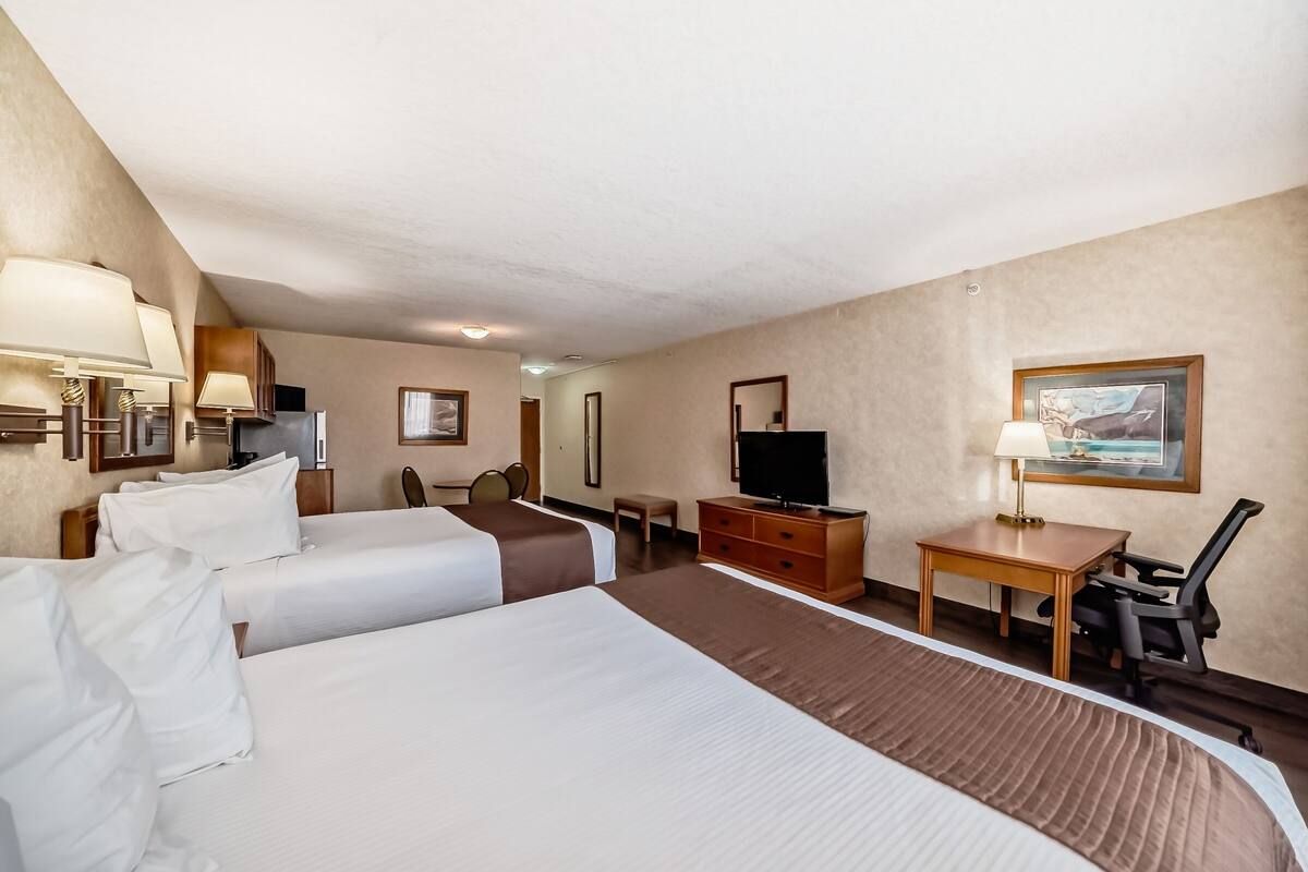 Une chambre d’hôtel avec deux lits, un bureau, une chaise, une télévision et un tableau au mur.