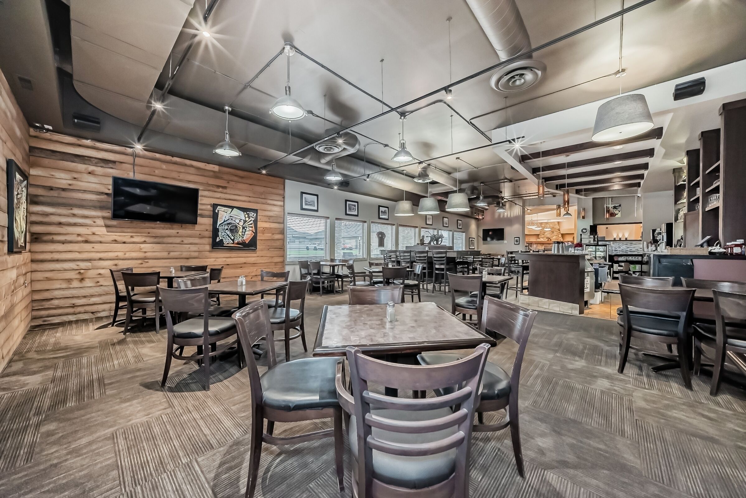 A spacious restaurant with wooden walls, multiple tables and chairs, and a modern ceiling design.