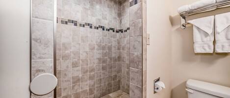 A bathroom with a shower area, a toilet, and a towel rack.