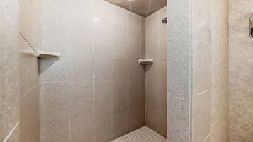 A small, tiled shower room with a grid floor and a corner showerhead.