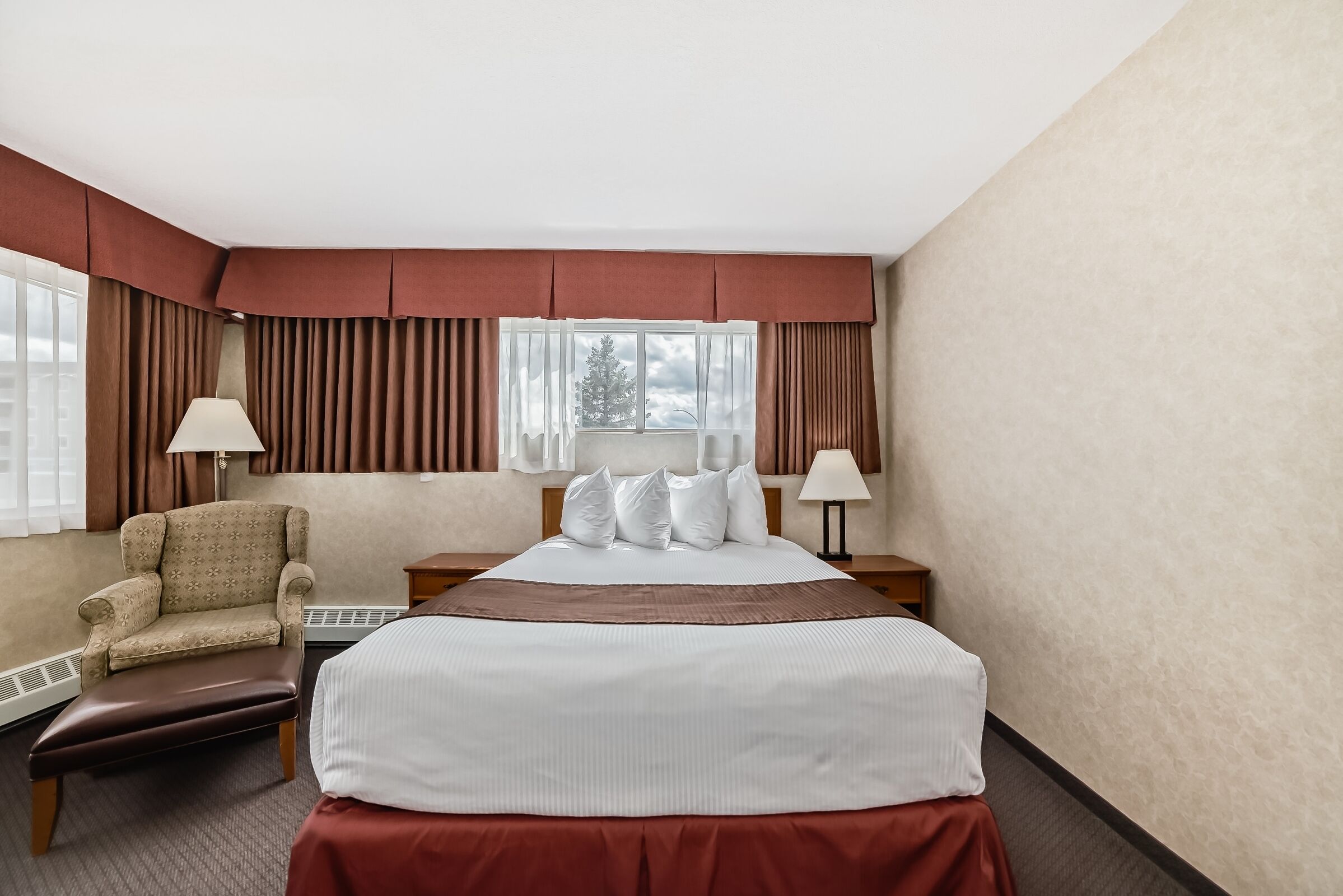 Habitación de hotel con cama, una silla, una mesita de noche y ventana con cortinas.