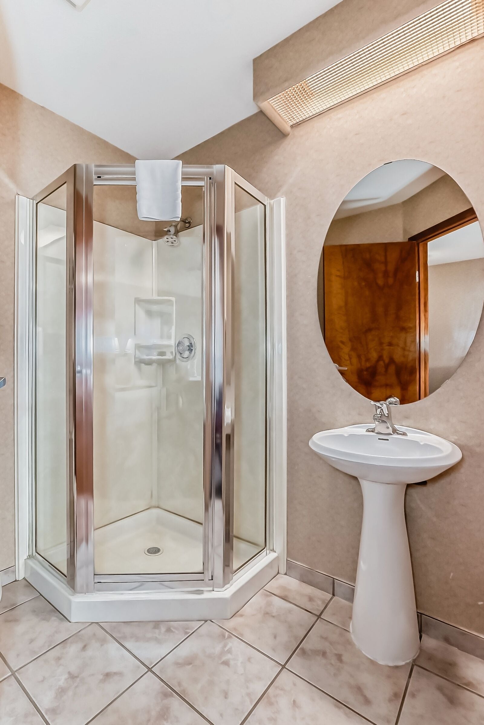 A modern bathroom with a glass-enclosed shower, a white pedestal sink, and a round mirror on the wall.
