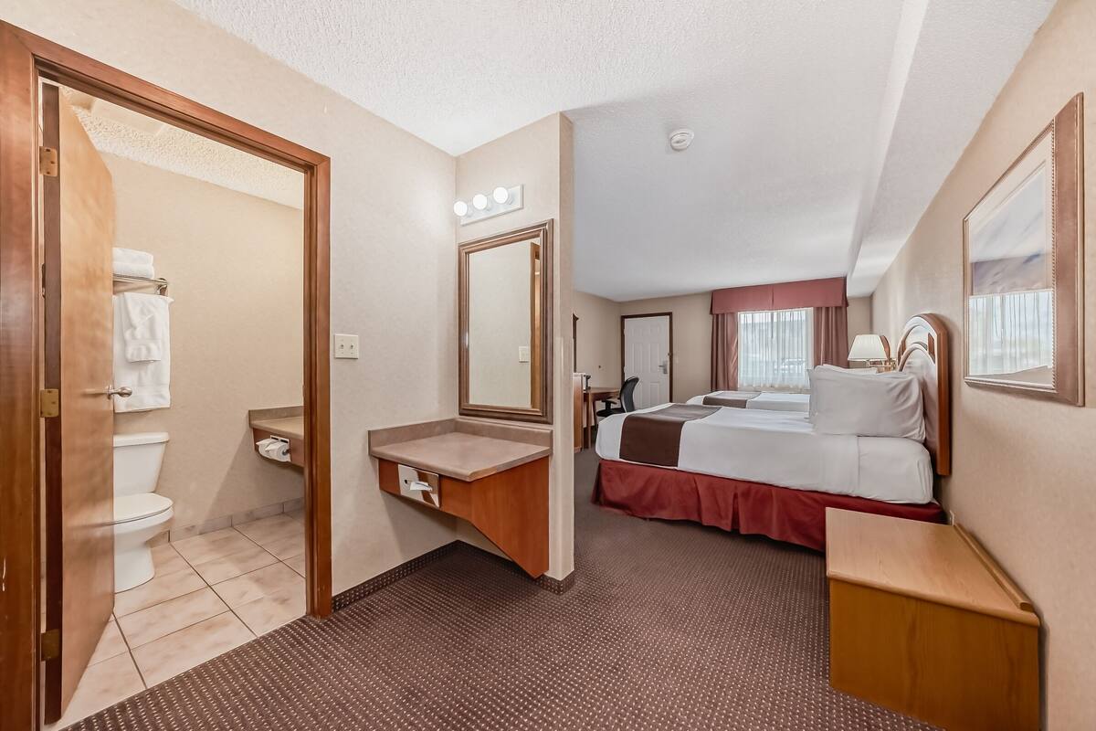 Une chambre d’hôtel avec une salle de bain, un lit avec une couvre-lit rouge, une coiffeuse avec un miroir et une table de chevet.