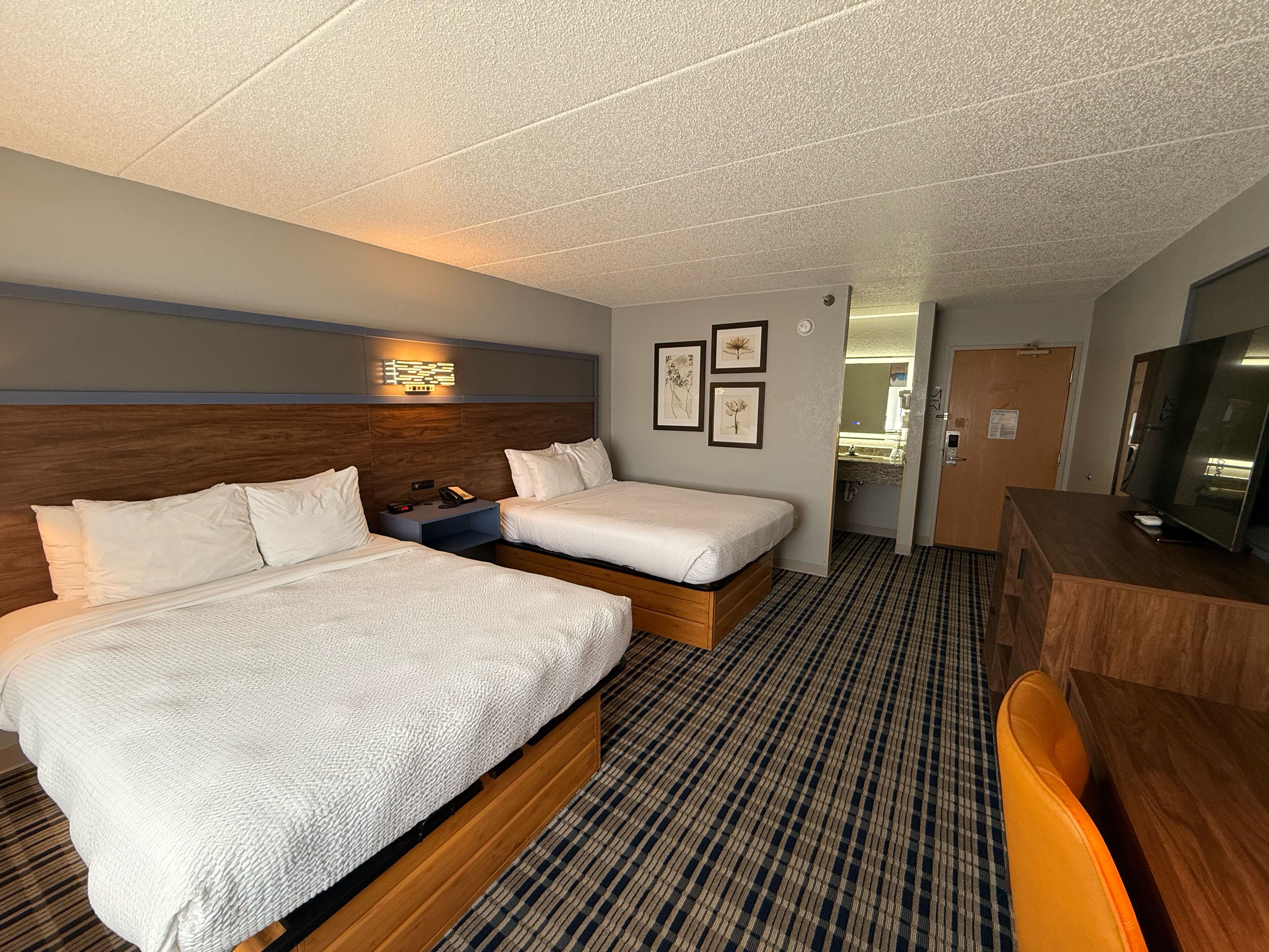 A hotel room with two beds, a desk, a TV, and a bathroom visible through an open door.