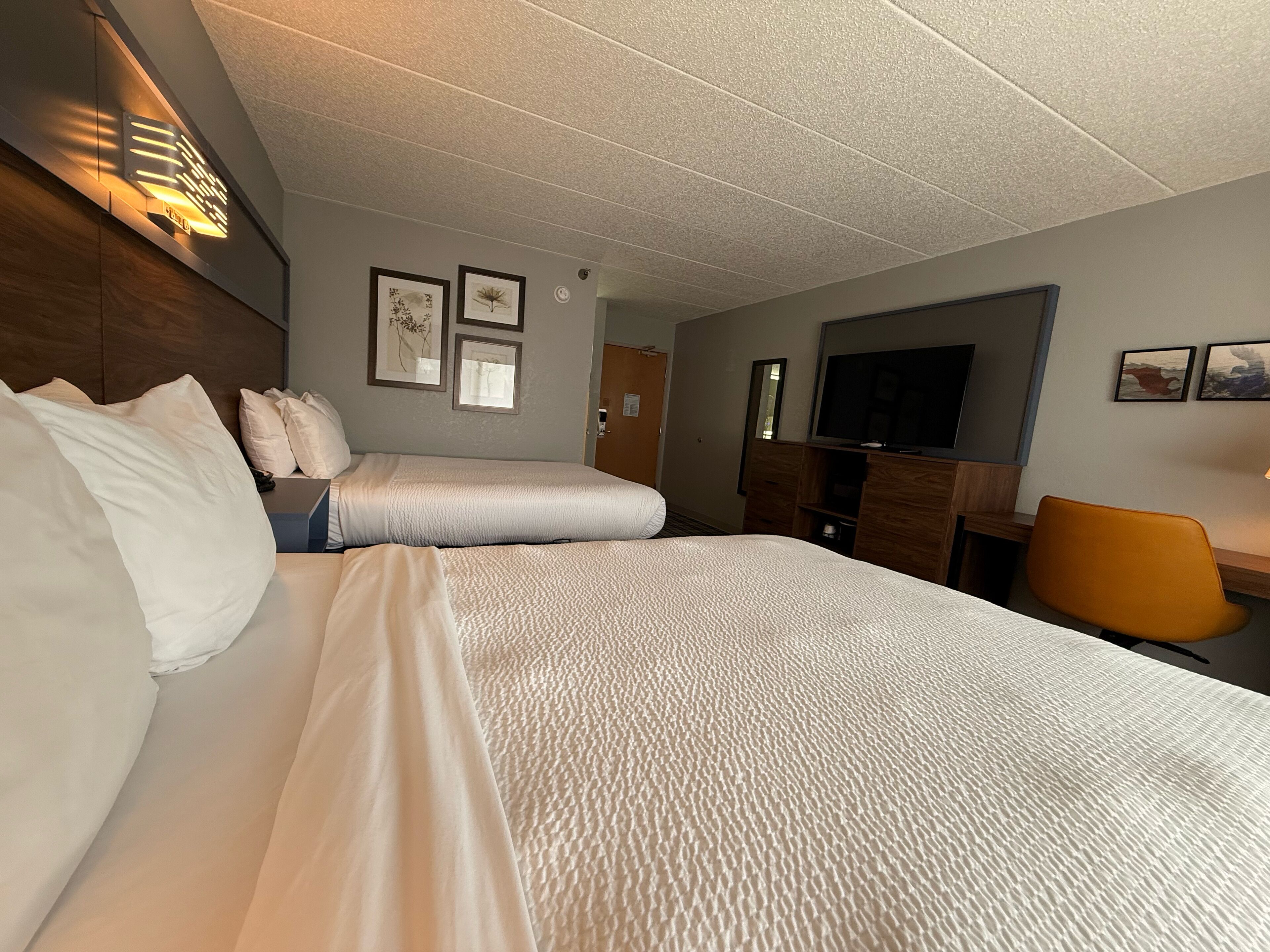 Une chambre d’hôtel avec un grand lit, un bureau avec une chaise, une télévision et des œuvres d’art accrochées aux murs.