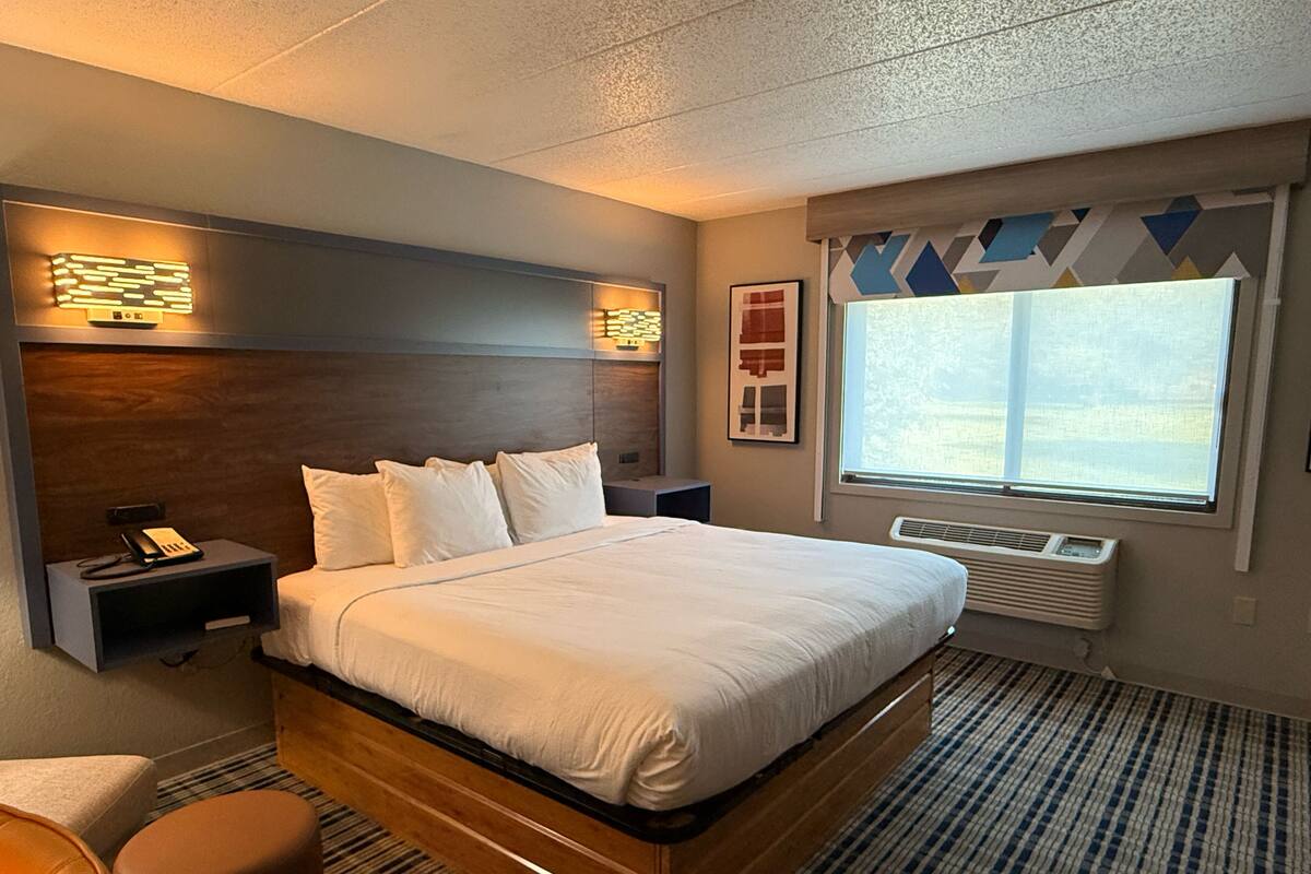 A hotel room with a large bed, bedside tables, a telephone, a window with a view, and a radiator.