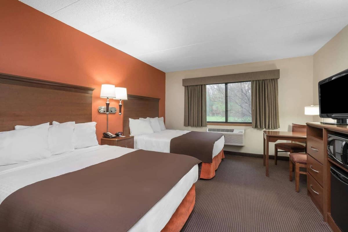 A hotel room with two beds, a desk, a television, and a window with curtains.
