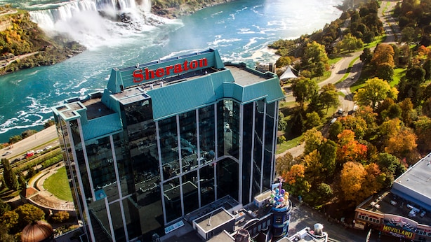 A Sheraton hotel with a glass facade, located near a waterfall and surrounded by autumn foliage. - Sheraton Fallsview Hotel (Niagara Falls)