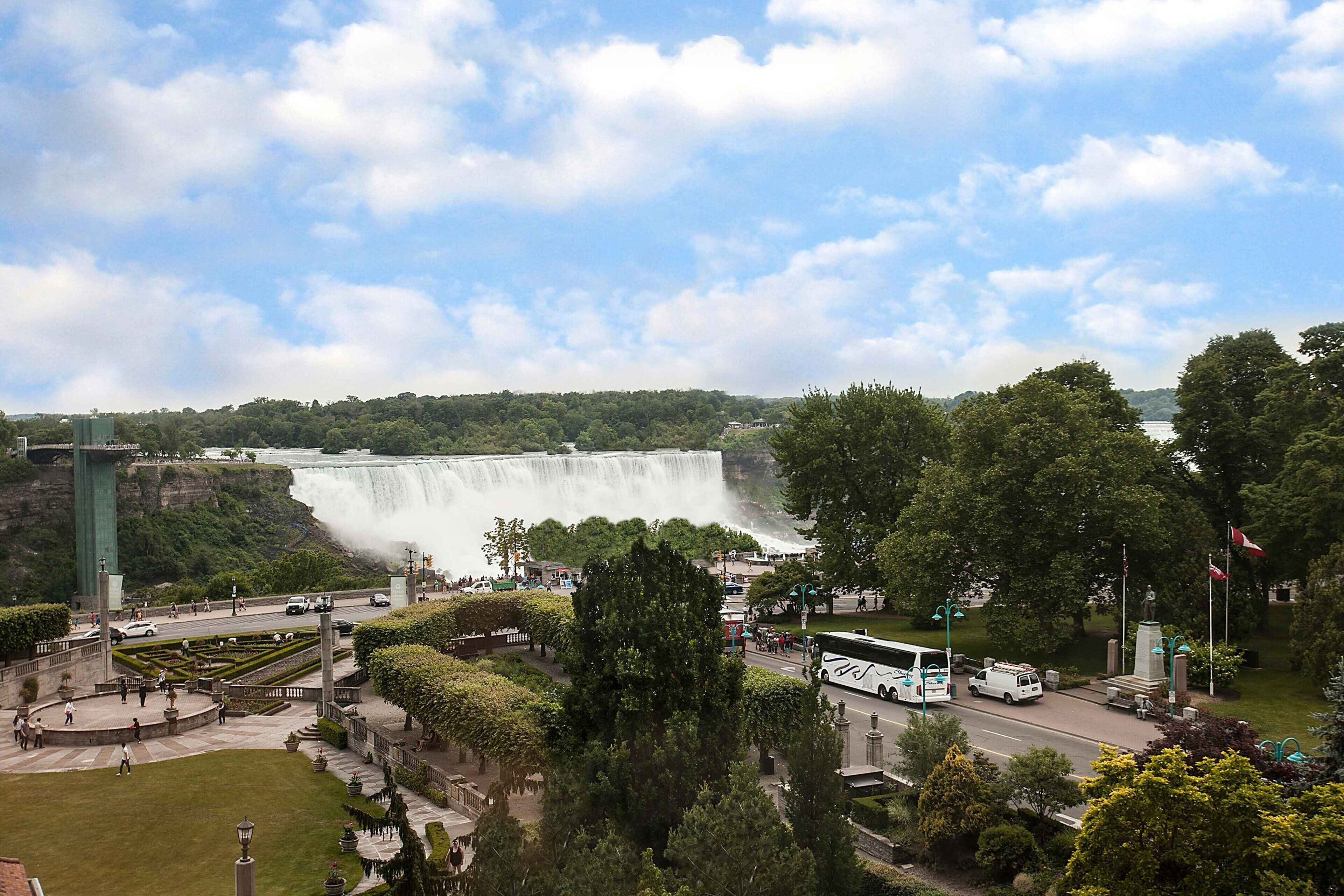 A view of a waterfall with a bridge and surrounding greenery.