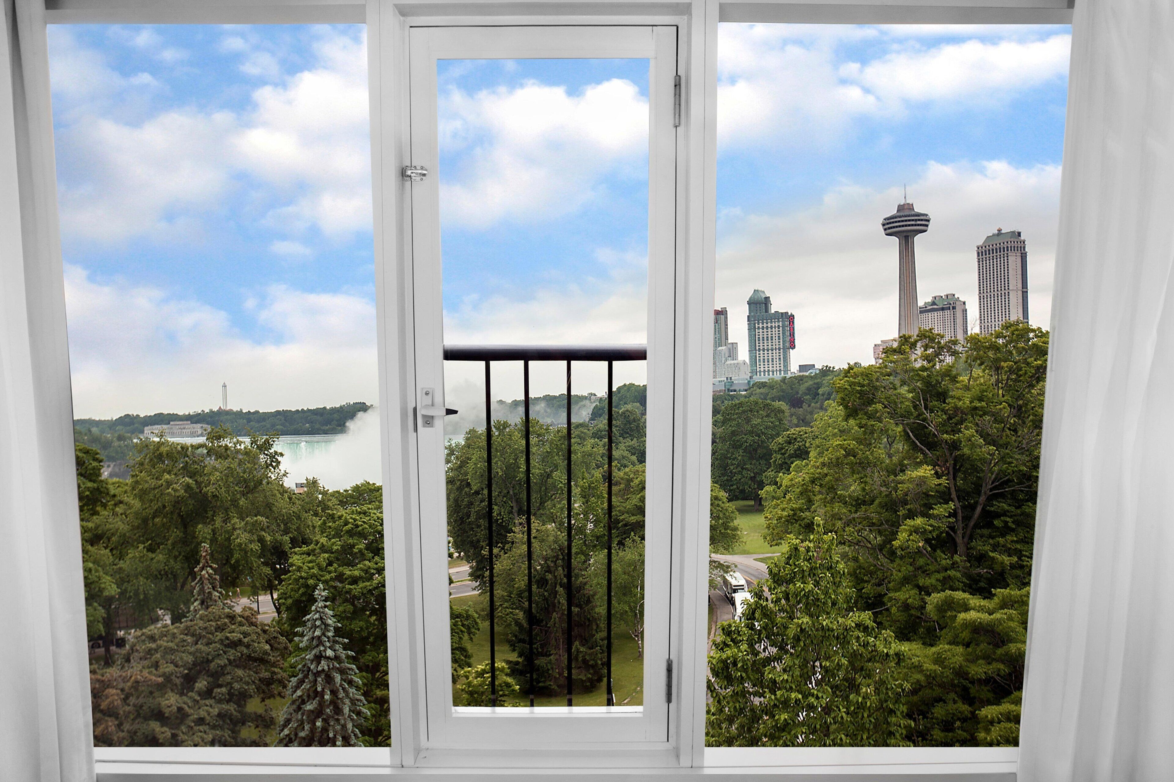 Vista a través de una ventana de marco blanco y barras negras, con vista a un paisaje urbano que destaca una torre y un cuerpo de agua.