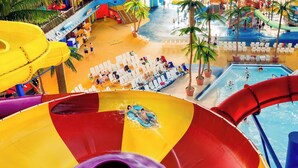 Un parc aquatique doté d’un grand toboggan multicolore, d’un espace piscine avec des chaises longues et de palmiers.