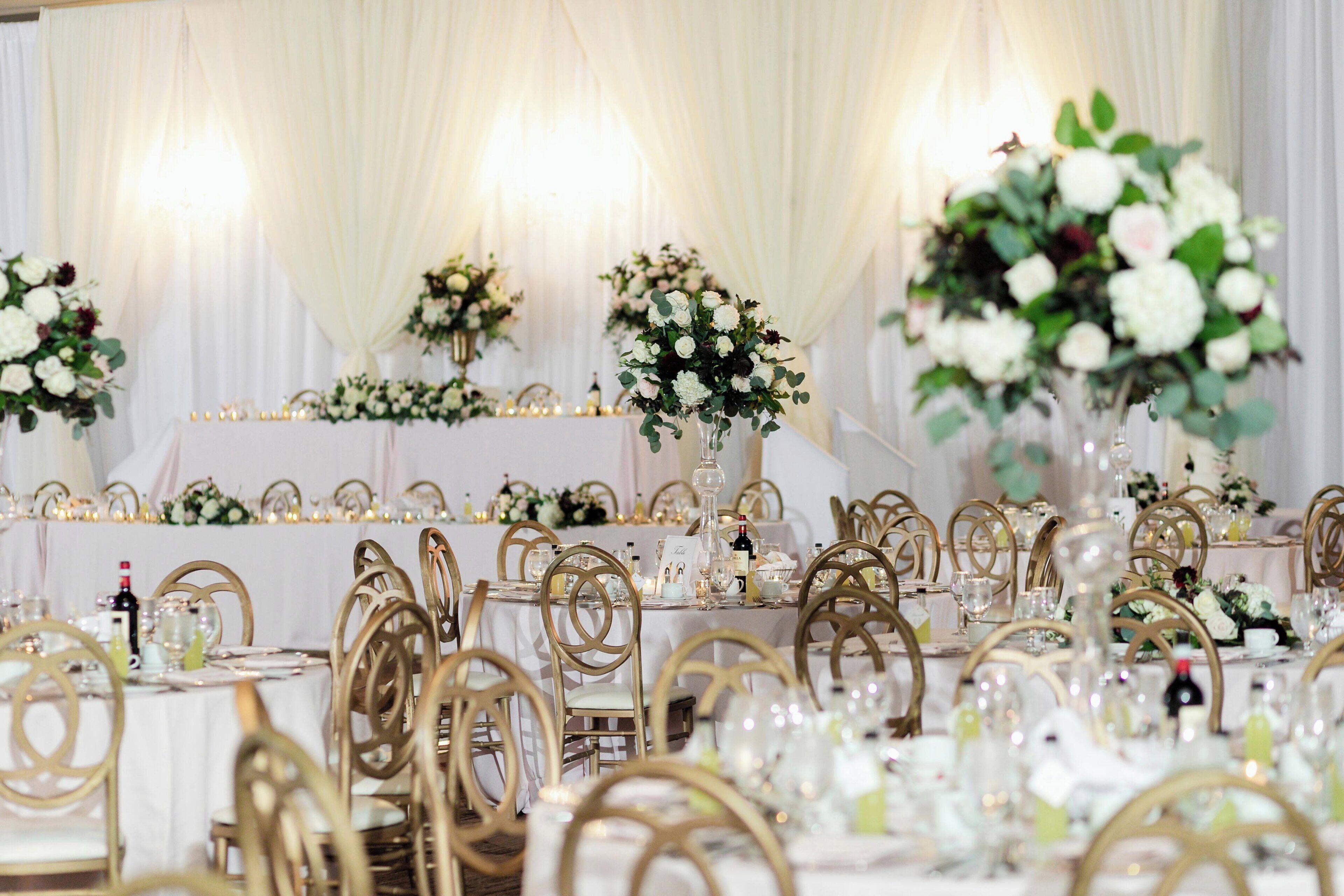 Une salle de banquet avec des tables rondes, des chaises dorées et des centres de table floraux.