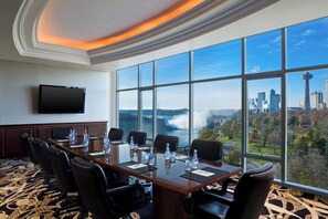 A conference room with a large table, chairs, and a view of a city skyline with a waterfall.