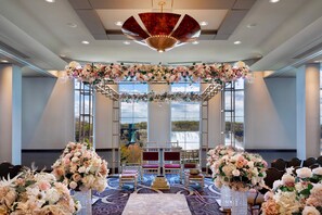 An indoor venue with a stage, chairs, and floral arrangements.