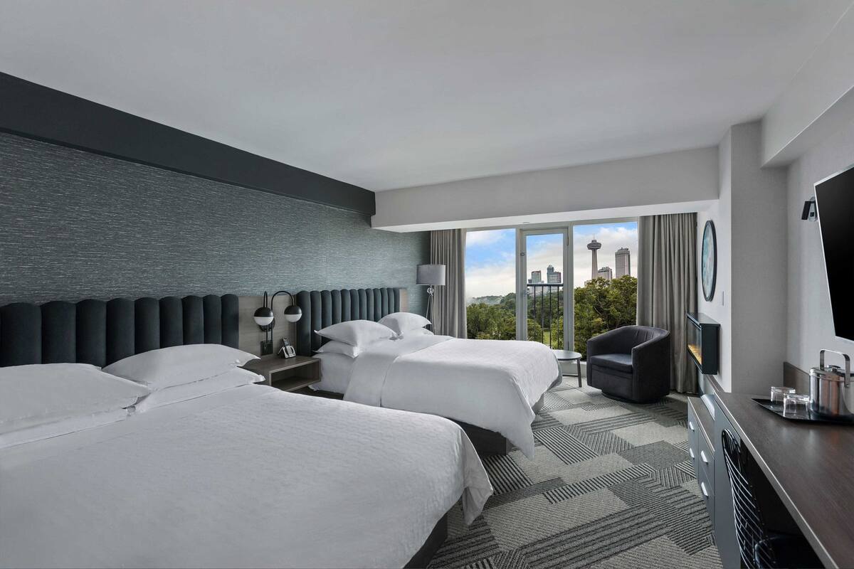 A hotel room with two beds, a sofa, a TV, and a city view.