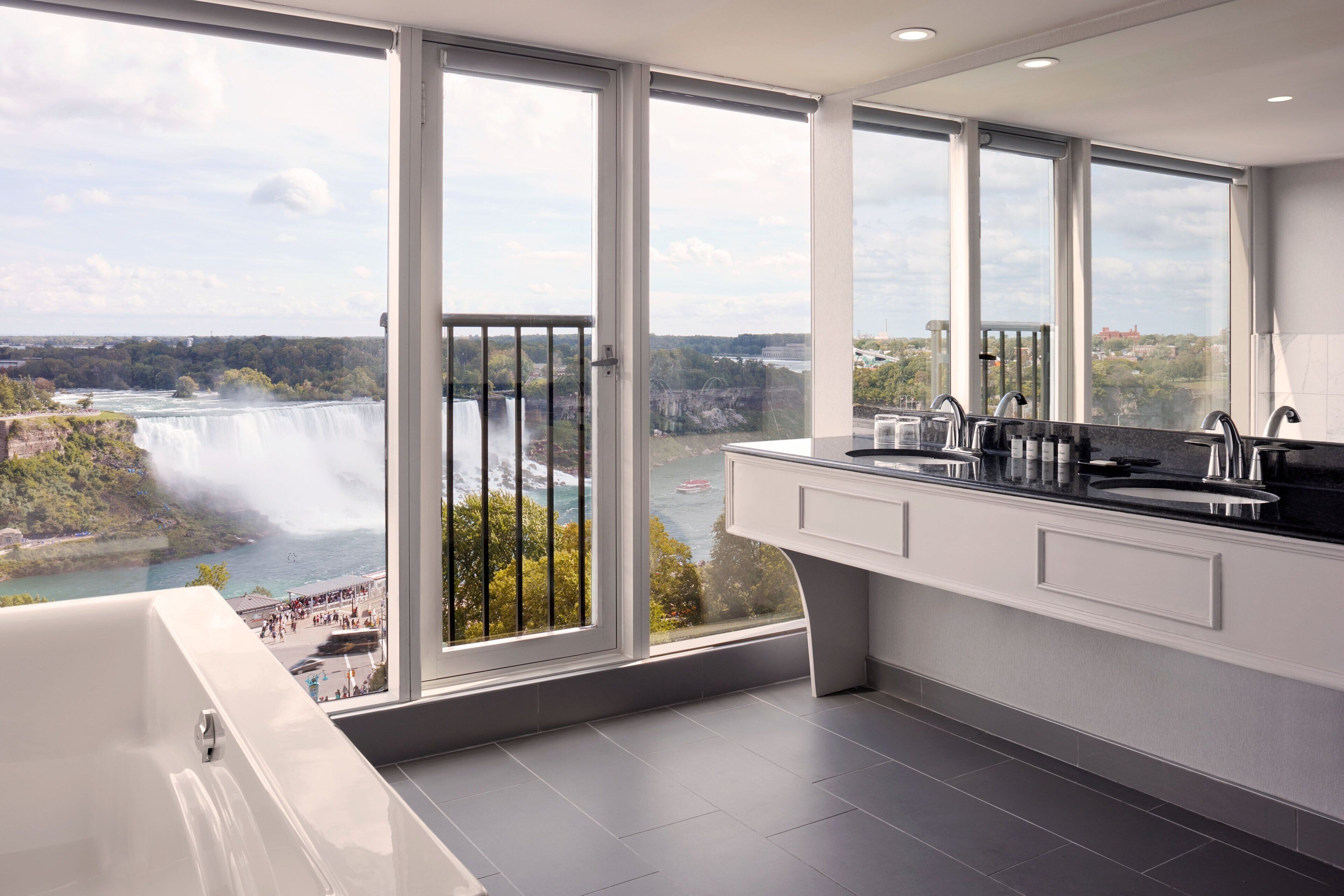 A modern bathroom with a large window overlooking a waterfall and a scenic view.