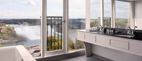 A modern bathroom with a large window overlooking a waterfall and a scenic view.