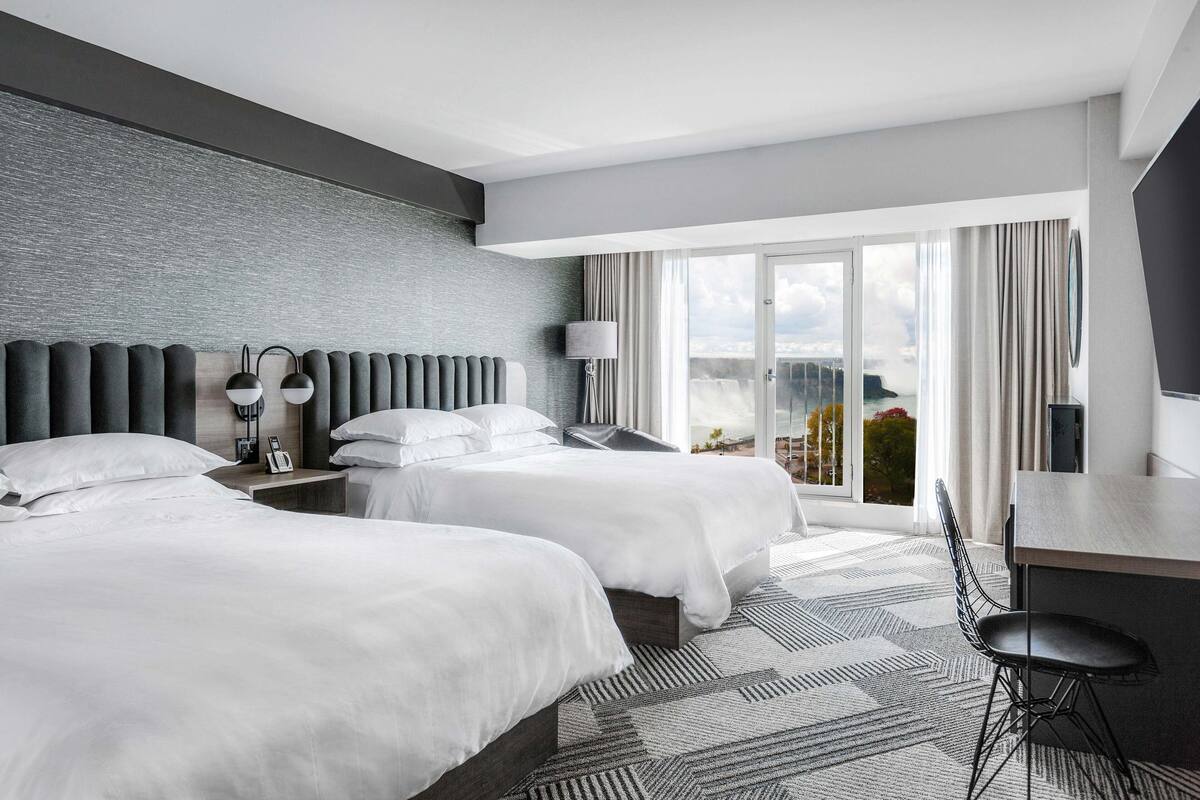 A hotel room with two beds, a desk, and a view of the city.