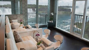Une chambre d’hôtel moderne dotée d’un grand balcon, de canapés en cuir blanc, d’une petite table et d’une orchidée en pot.
