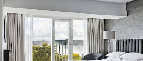 A modern hotel room with a large window, a bed, a chair, and a lamp.