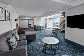 A modern hotel lobby with a gray sofa, a round table, and a large TV screen.