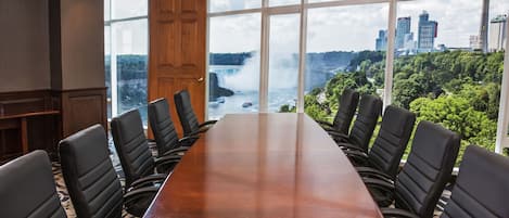 Un salón de conferencias con una larga mesa y sillas negras, ventanas amplias con vistas a la ciudad y a una cascada.