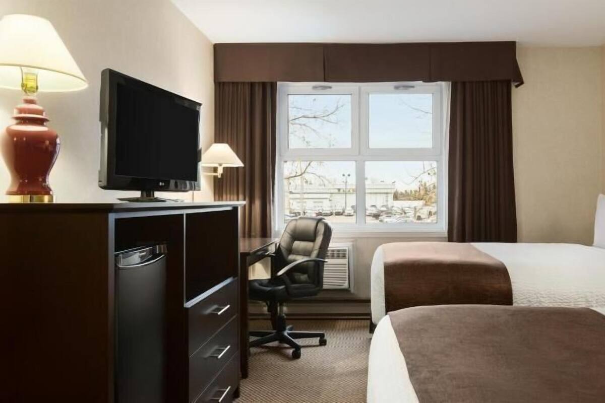 A hotel room with a bed, a desk with a chair, a television, and a window with curtains.