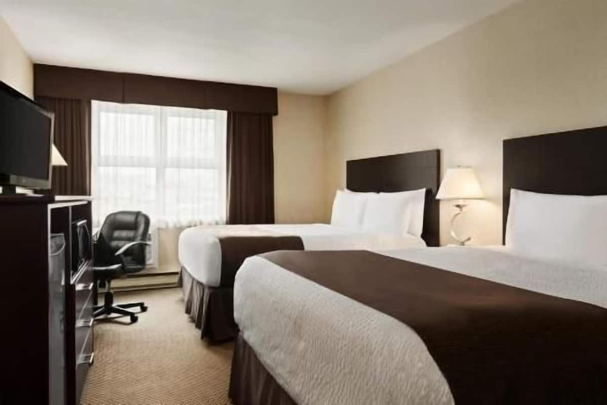 A hotel room with two beds, a desk, a chair, and a TV.