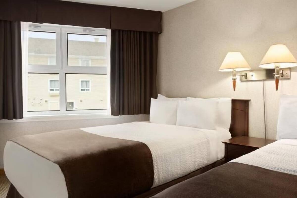 A hotel room with two beds, a window with curtains, and two wall-mounted lamps.