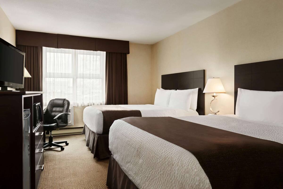 A hotel room with two beds, a desk with a computer, a chair, and a window with curtains.