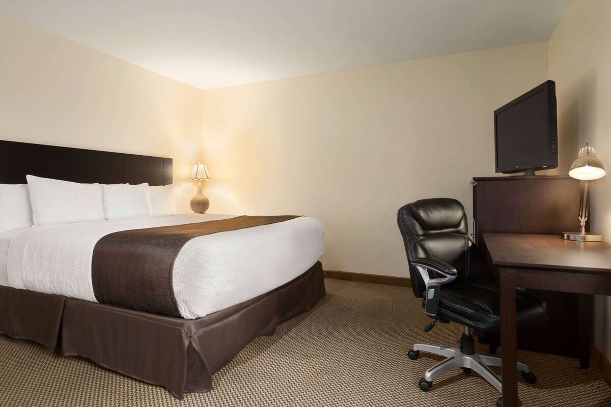 A hotel room with a large bed, a desk with a computer, a chair, and a TV.
