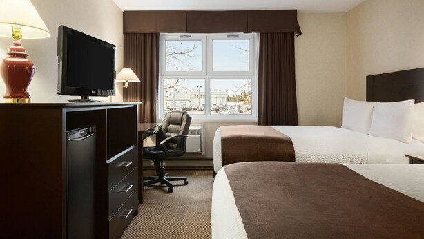 A hotel room with a bed, a desk with a television, a chair, and a window with curtains. - Days Inn by Wyndham Trois-Rivieres (Trois-Rivieres)