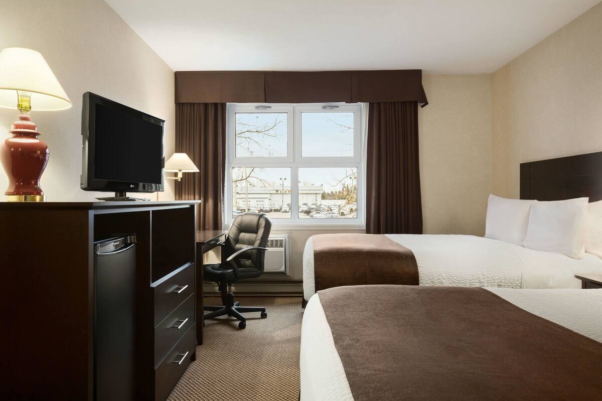 A hotel room with a bed, a desk with a television, a chair, and a window with curtains.