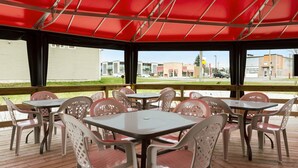 An outdoor patio with tables and chairs, a red canopy, and a view of buildings in the background. - Days Inn by Wyndham Trois-Rivieres (Trois-Rivieres)