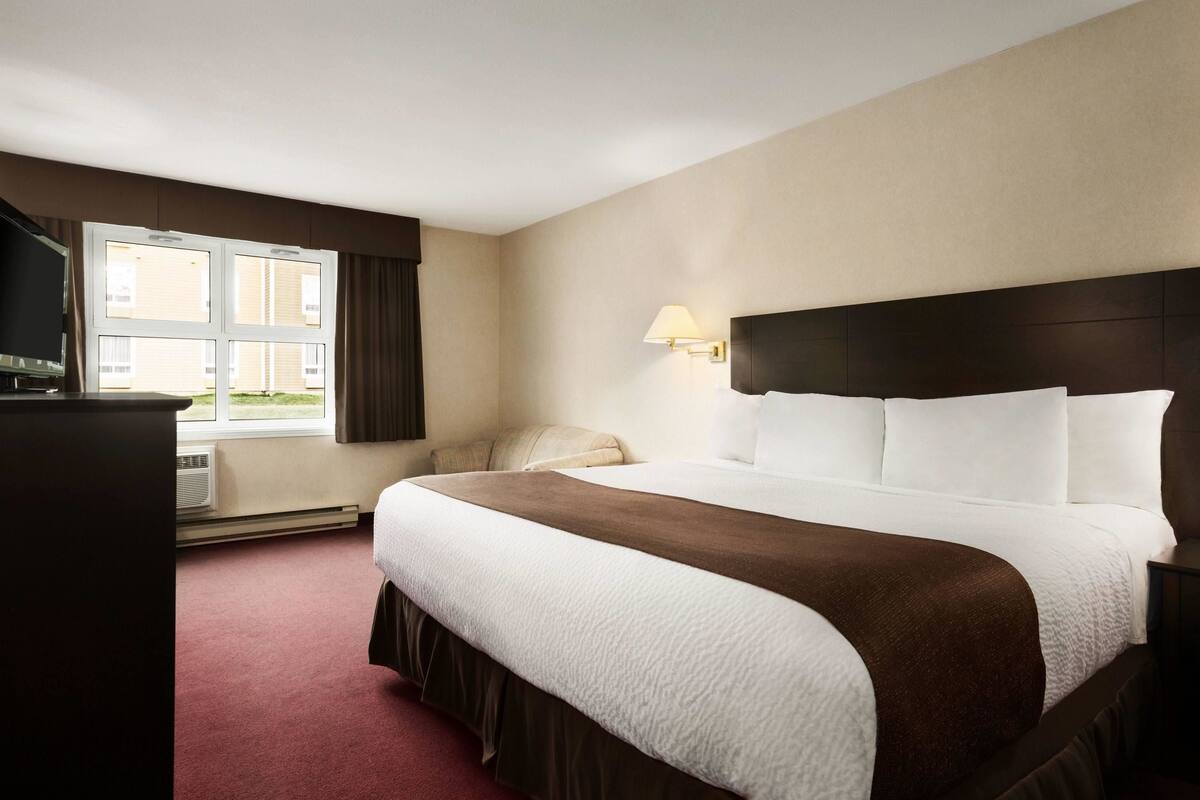 A hotel room with a large bed, a TV, a window, and a lamp.