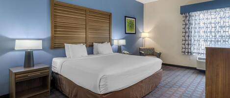 A hotel room with a large bed, two bedside tables with lamps, a wooden headboard, a patterned carpet, and a window with a curtain.