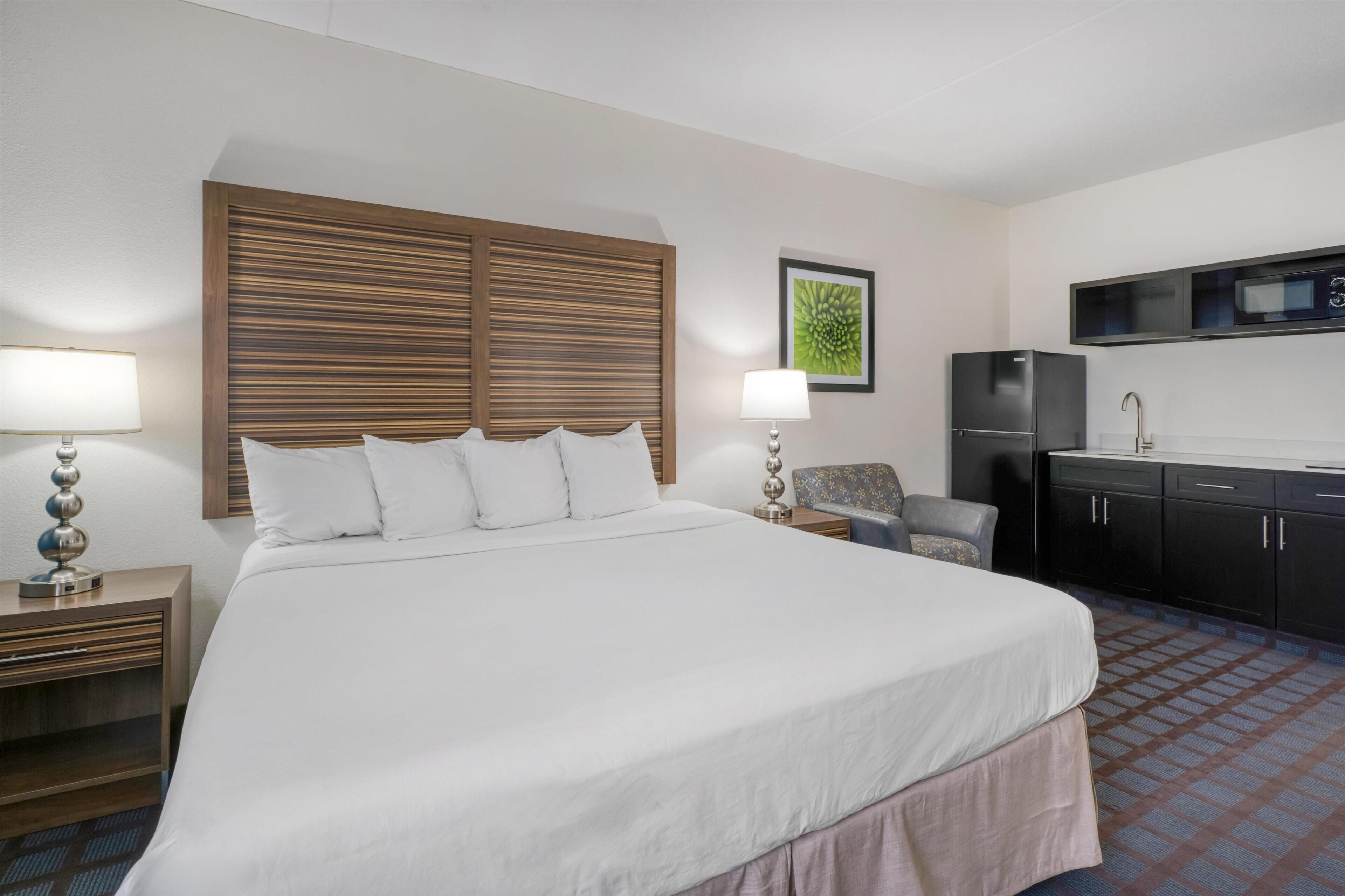 A hotel room with a large bed, a desk, a chair, a microwave, and a refrigerator.